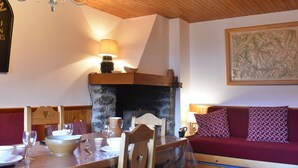 A cozy room with a wooden ceiling, a stone fireplace, a dining table set with plates and glasses, a sofa with patterned cushions, and a map on the wall. - Bright apartment near slopes - 6 guests (Méribel)