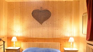 A wooden-paneled room with a bed, two bedside tables with lamps, and a heart-shaped wall decoration. - Bright apartment near slopes - 6 guests (Méribel)