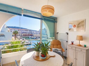 Ein Balkon mit Tisch, Stühlen, Topfpflanzen, einer Hängeleuchte und Blick auf einen Jachthafen und Gebäude.