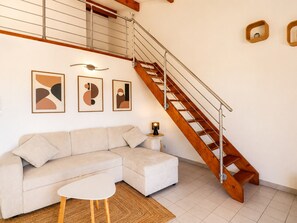 A modern living room with a wooden staircase, a sofa, a small table, and abstract wall art. - Spacious T3, terrace mountain view - 6 guests (Sète)