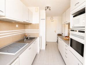 A kitchen with white cabinets, a stainless steel sink, a built-in oven, and a microwave. - Spacious T3, terrace mountain view - 6 guests (Sète)