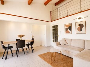 A modern living room with a sofa, a dining table with chairs, a small white table, and abstract wall art. - Spacious T3, terrace mountain view - 6 guests (Sète)