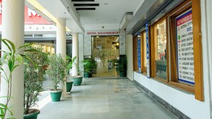 Entrada de un hotel con puerta de vidrio, plantas en macetas y un cartel de una tienda cercana.