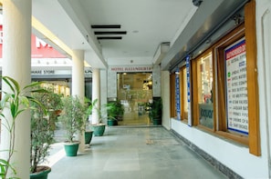 A hotel entrance with a glass door, potted plants, and a sign for a nearby store. - Hotel Jullundur 18 (Chandigarh)