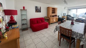 Ein Wohnzimmer mit einem roten Sofa, einem Esstisch mit Stühlen, einem Holzschrank und einer roten Lampe.