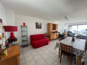 Ein Wohnzimmer mit einem roten Sofa, einem Esstisch mit Stühlen, einem Holzschrank und einer roten Lampe.