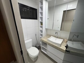 A bathroom with a white toilet, a sink with a granite countertop, and a mirror above the sink.