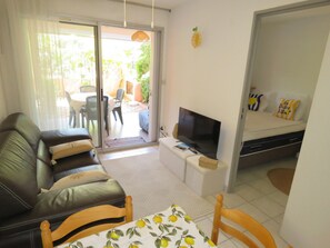 A living room with a sofa, TV, and a table with a lemon pattern. - T2 cabin apartment with AC, garden & parking (Sète)