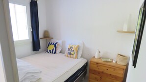 Une chambre à coucher avec un lit, une table de chevet en bois, une fenêtre avec des rideaux et une étagère fixée au mur.