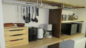 Une cuisine compacte avec des meubles en bois, une machine à café, un four à micro-ondes et des ustensiles de cuisine accrochés au mur.