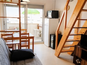 Ein kompakter Wohnraum mit Sofa, Esstisch, Stühlen, einem Fernseher und einer Holztreppe.