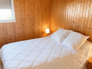 Ein Bett mit gesteppter weißer Bettdecke, einer Nachttischlampe und Holzvertäfelung.