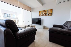 Ein modernes Wohnzimmer mit Ledersofas, einem Flachbildfernseher und einem Gemälde an der Wand.