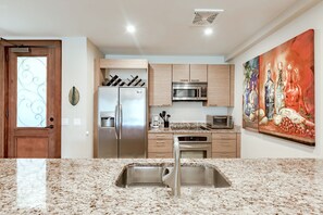 Eine moderne Küche mit Granit Arbeitsplatten, Edelstahlgeräten und einem großen Gemälde an der Wand.