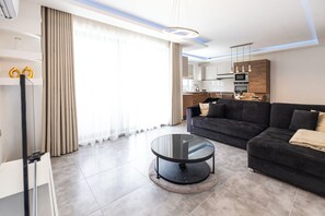 Ein modernes Wohnzimmer mit einer Couch, einem Glastisch und einer Küche im Hintergrund.