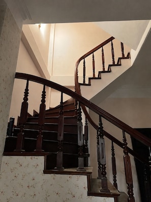 Uma escada de madeira com corrimão, degraus carpetados e parede com papel de parede floral.