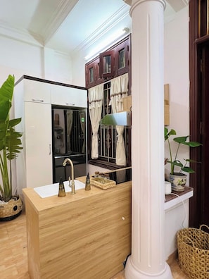 Un baño con tocador de madera, un lavabo y un espejo. Hay una planta en maceta sobre la encimera y una ventana con cortinas.