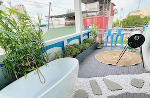 Terraço no telhado com banheira, cadeiras azuis, churrasqueira e plantas em vasos.