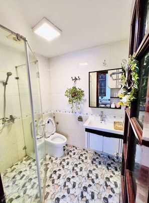A bathroom with a glass shower enclosure, a toilet, a sink with a mirror, and a decorative plant. - LushStay Hanoi Train Station (Cua Nam)