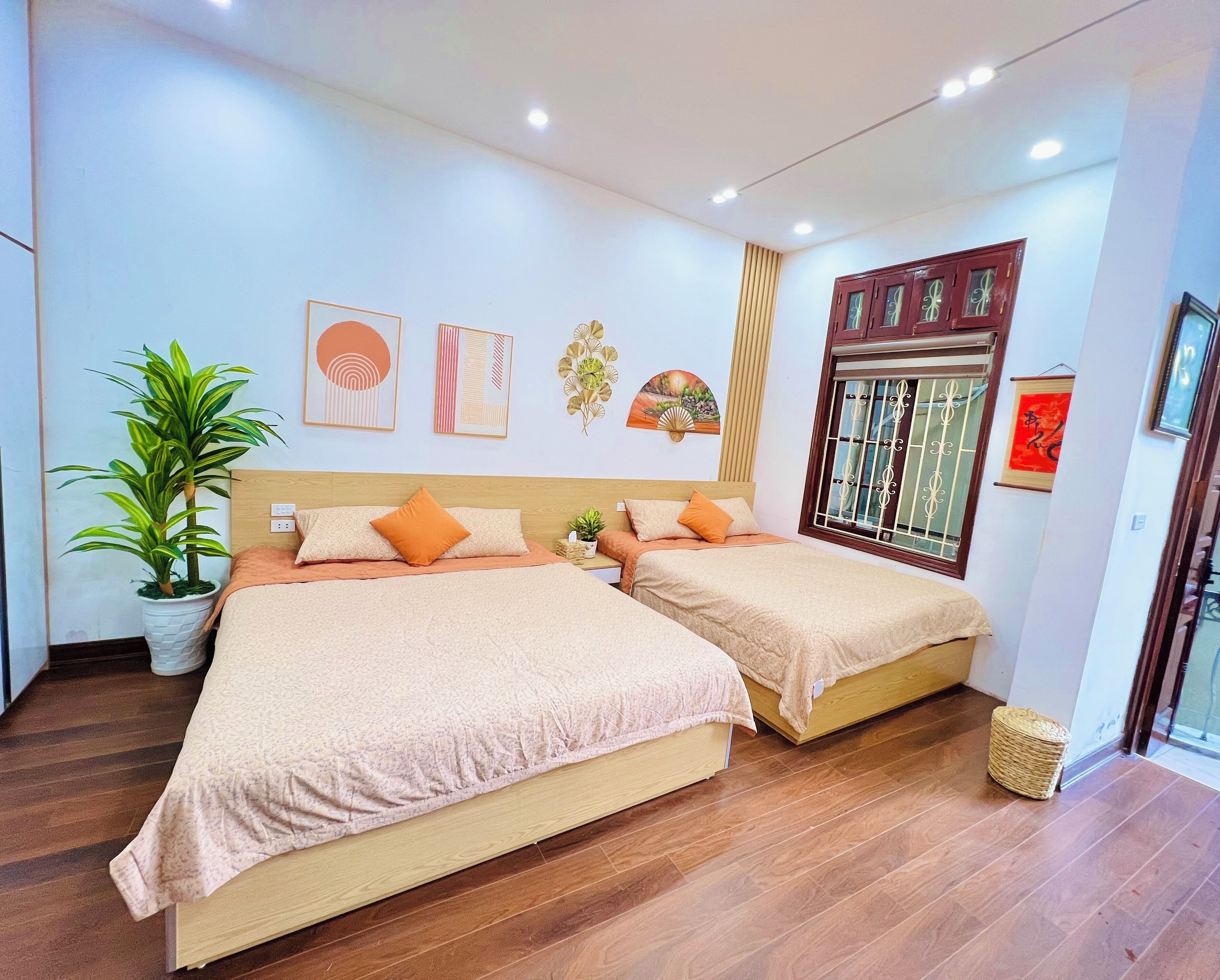 A hotel room with two beds, a potted plant, artwork on the walls, and a window with decorative bars.