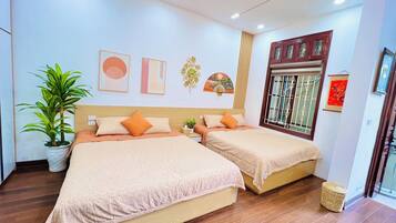 A hotel room with two beds, a potted plant, artwork on the walls, and a window with decorative bars.