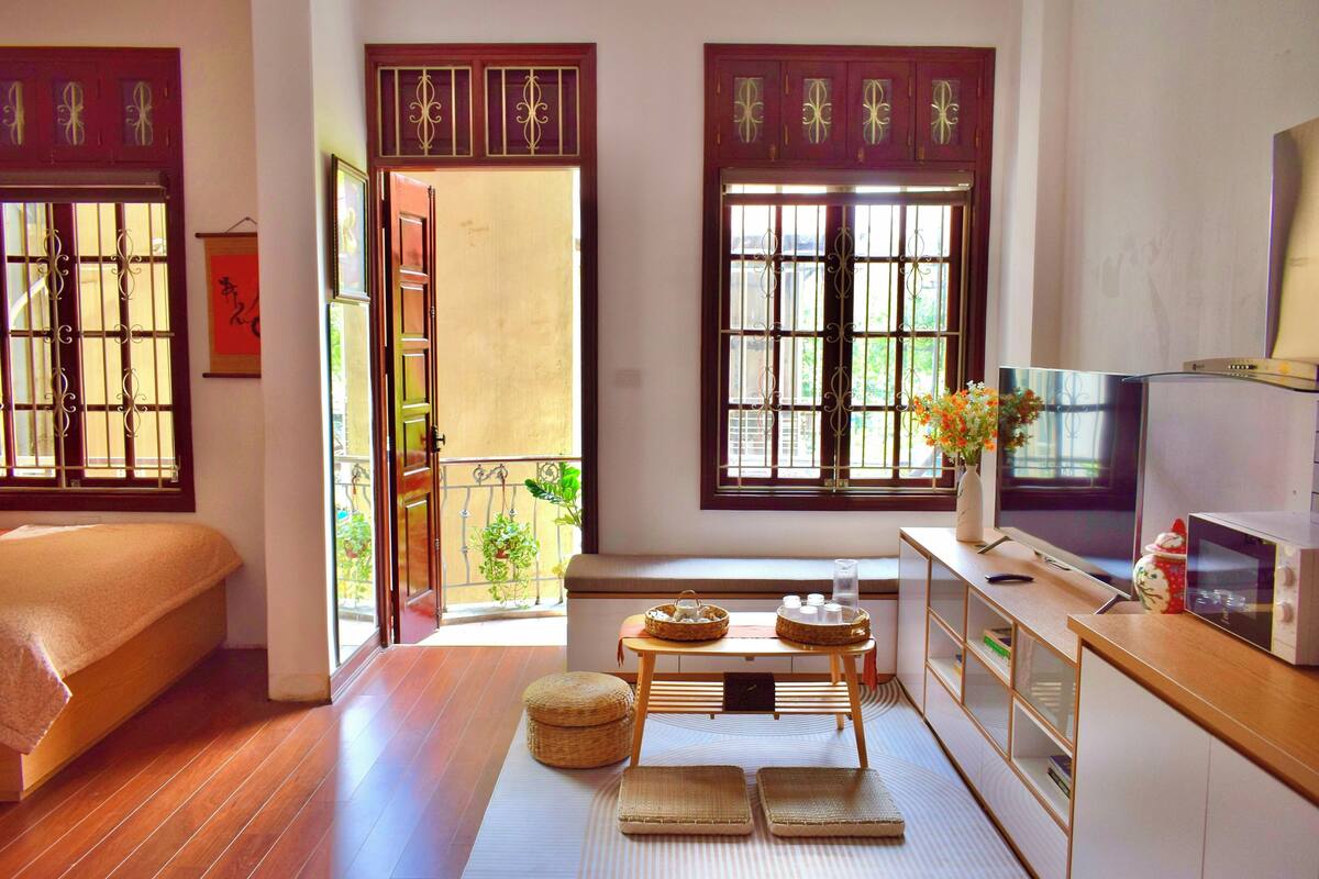 A room with a bed, a TV, a small table with items, and a view of the outside.