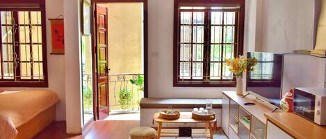A room with a bed, a TV, a small table with items, and a view of the outside.