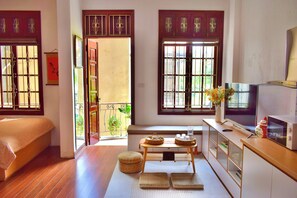 Una habitación con cama, televisión, una mesita con objetos y vistas al exterior.