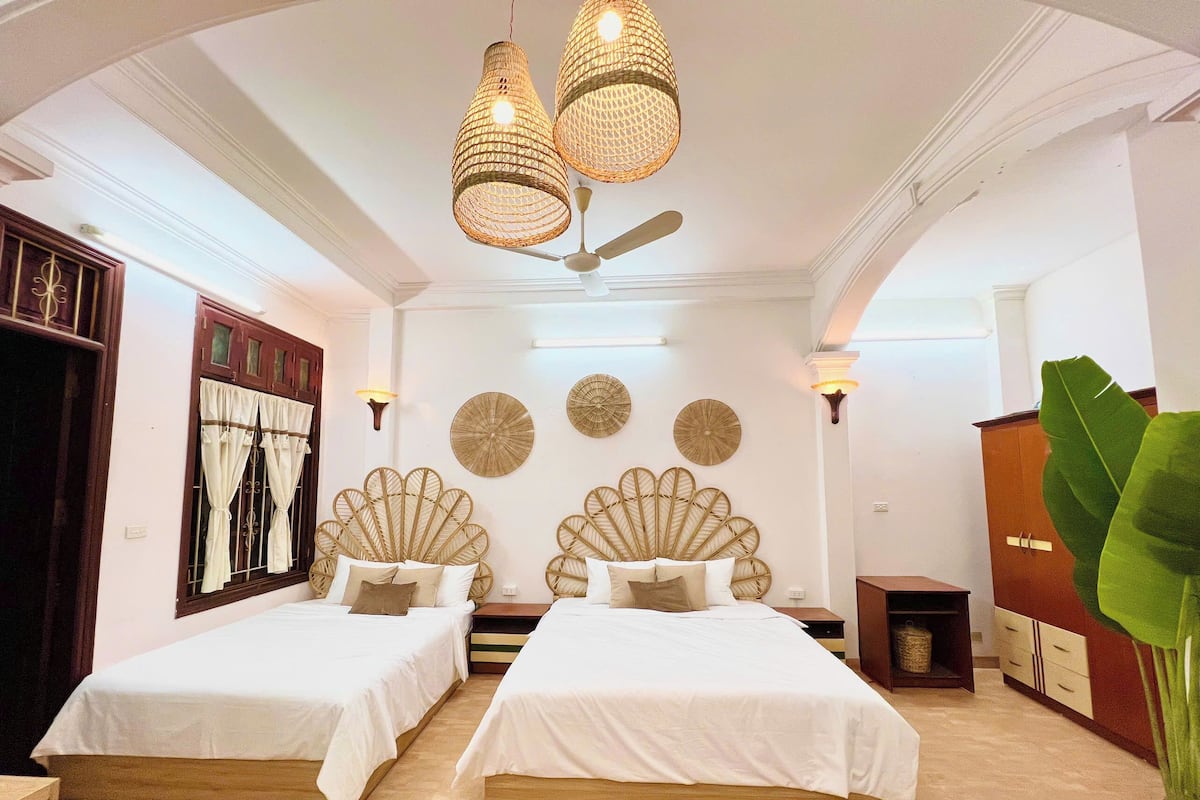 A hotel room with two beds, a ceiling fan, decorative wall art, and a large plant.