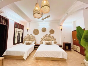 A hotel room with two beds, a ceiling fan, decorative wall art, and a large plant. - LushStay Hanoi Train Station (Cua Nam)