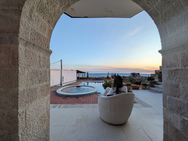 Un arc en pierre mène à une terrasse sur le toit, dotée d’une piscine, de coins salon extérieurs et offrant une vue sur la mer au coucher du soleil.
