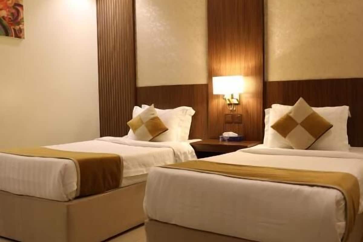 A hotel room with two beds, a nightstand, a lamp, and a wall-mounted artwork.