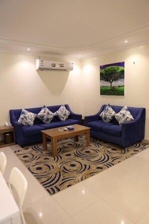 Uma sala de estar com dois sofás azuis, uma mesa de centro de madeira e um tapete estampado.