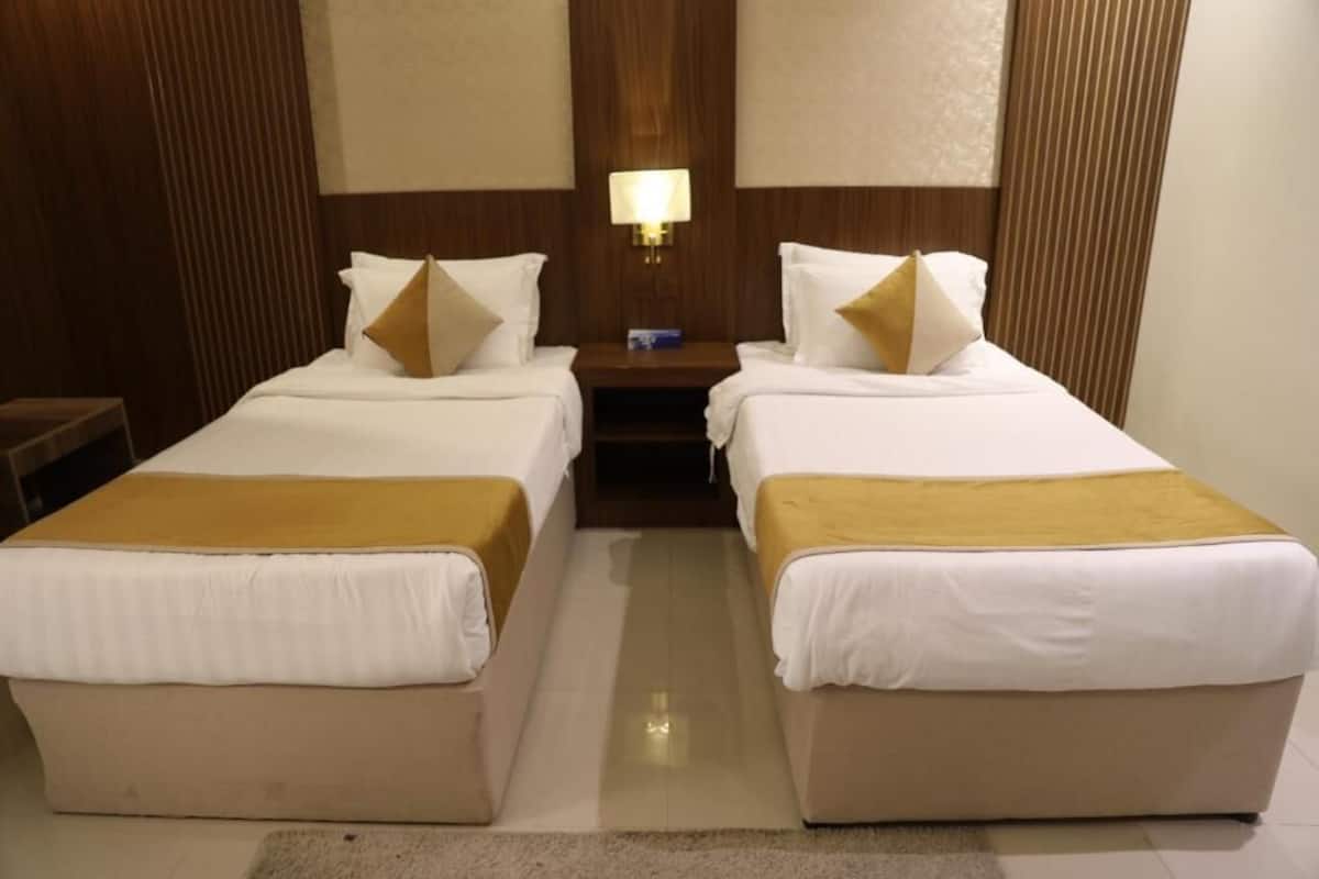 A hotel room with two beds, a nightstand with a lamp, and a wooden headboard.