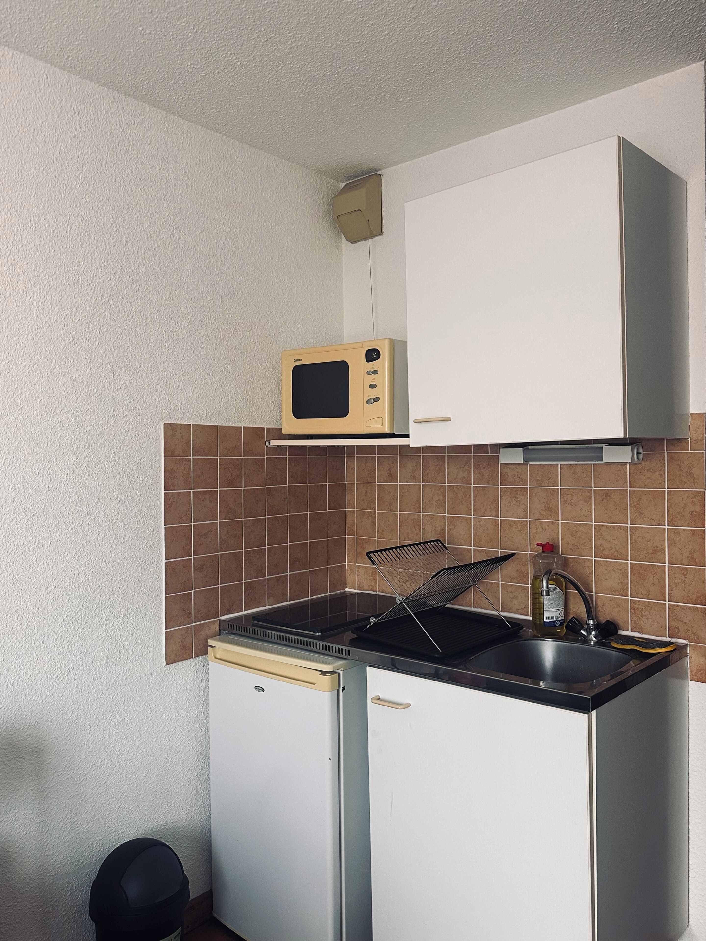 Cocina compacta con microondas, lavamanos y un refrigerador pequeño.
