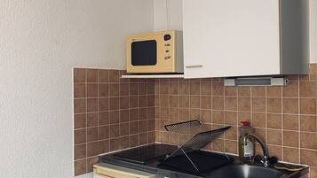Cocina compacta con microondas, lavamanos y un refrigerador pequeño.