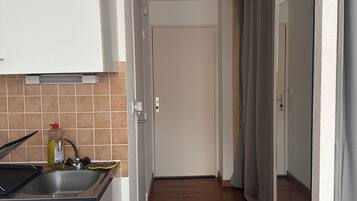 Un couloir étroit, avec une cuisine d’un côté, un plancher en bois et une porte au fond.