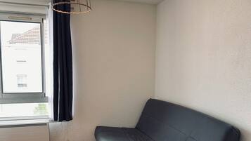 Une pièce avec un canapé gris foncé, un plancher en bois, une fenêtre avec des rideaux et un luminaire suspendu.