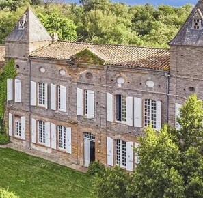 A multi-story stone building with a tiled roof, white shutters, and a tower. - Estate for rent from May through October (31560 Gibel)