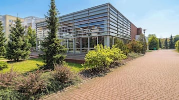 Um edifício moderno com fachada de vidro, cercado por vegetação e um calçada pavimentada.