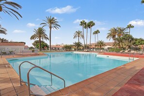 A swimming pool with clear blue water, surrounded by palm trees and a tiled deck. - Holiday Apartment 'Los Porches K28' with Shared Pool, Private Terrace & Wi-Fi (Maspalomas)
