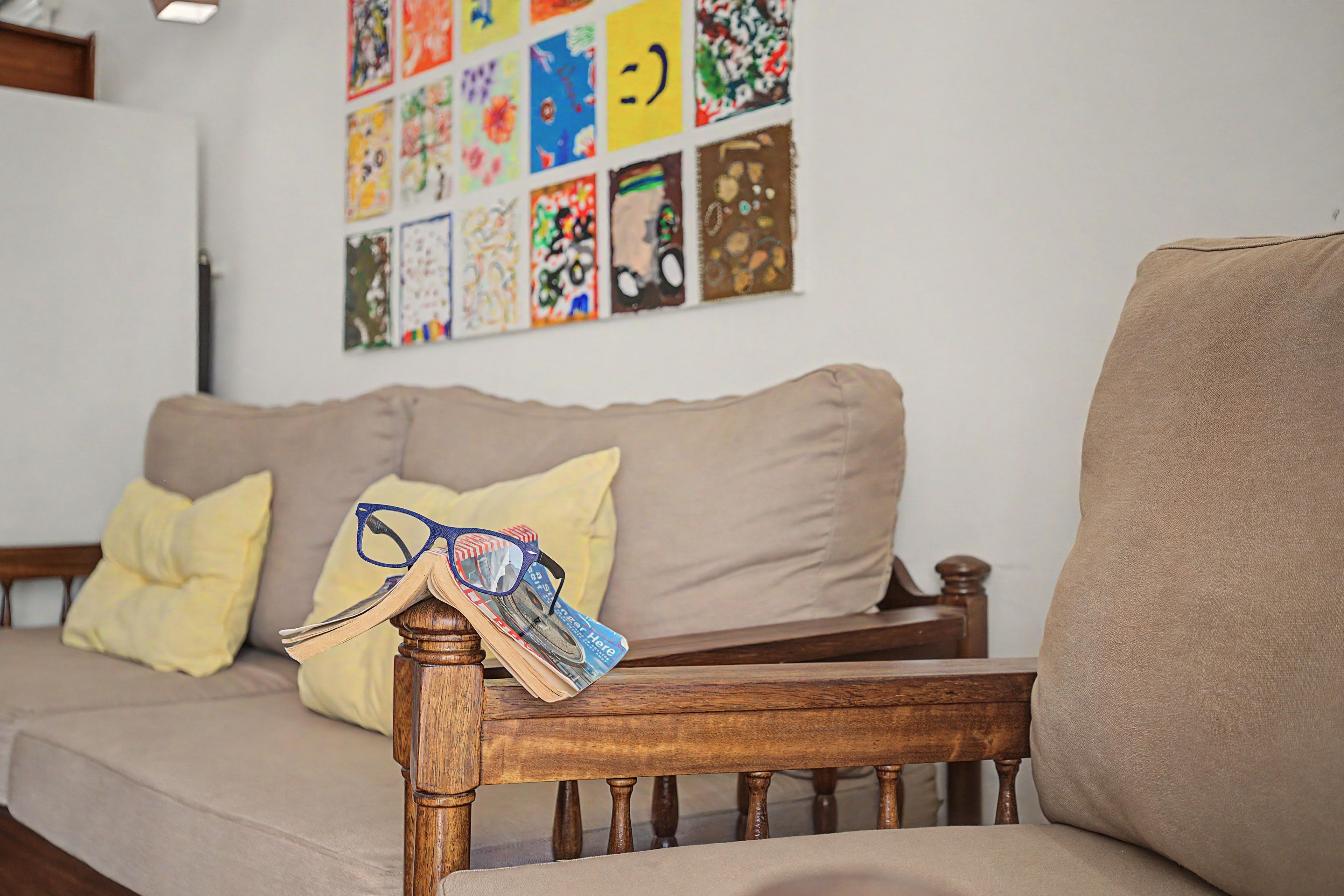 Ein Wohnzimmer mit einem Holzstuhl, einer Couch und einer Wand, die mit farbenfrohen Kunstwerken geschmückt ist.