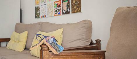 Ein Wohnzimmer mit einem Holzstuhl, einer Couch und einer Wand, die mit farbenfrohen Kunstwerken geschmückt ist.