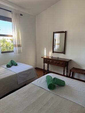 Ein Hotelzimmer mit zwei Betten, einer Holzkommode, einem Spiegel und einem Fenster mit Vorhängen.