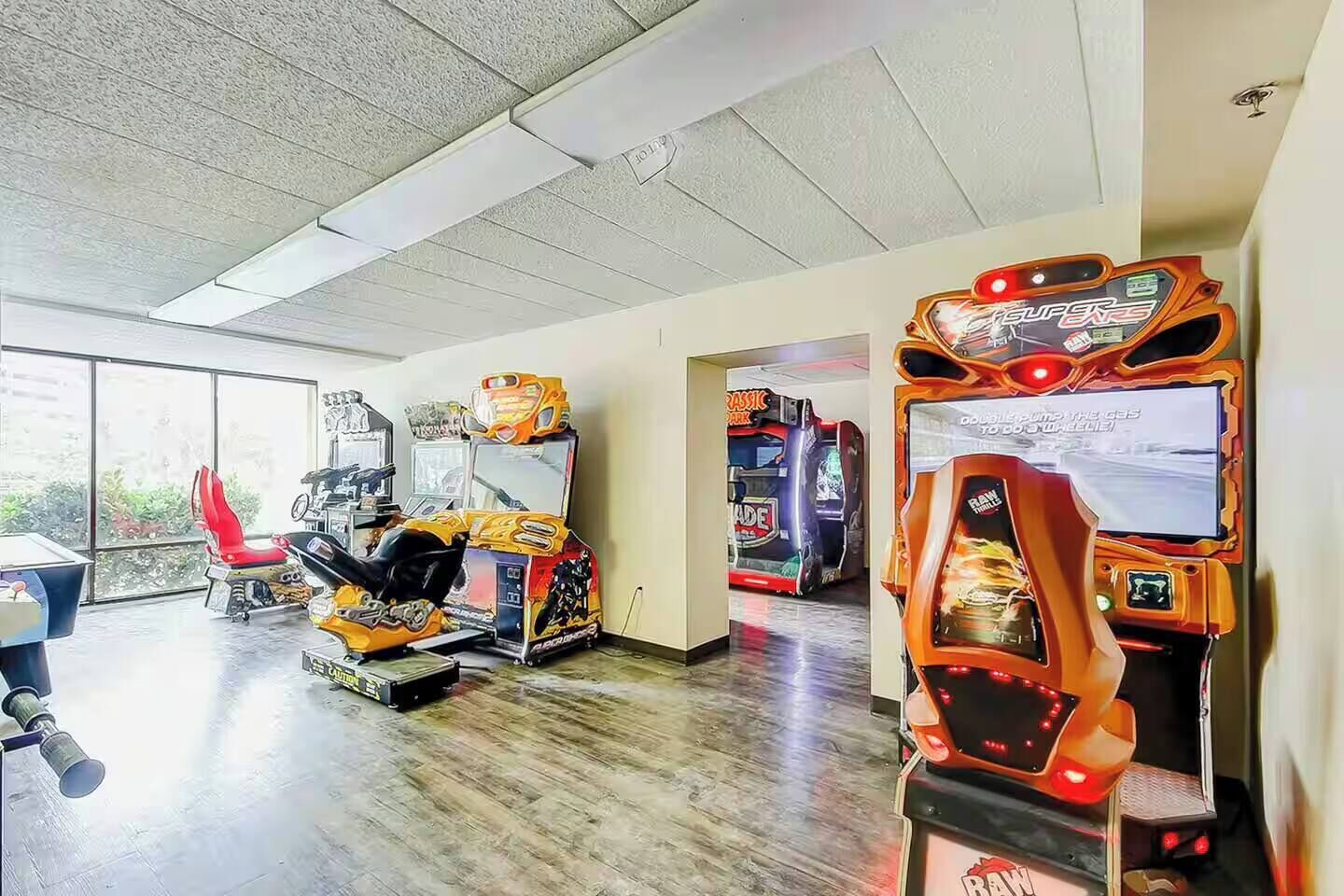 An indoor arcade with various gaming machines, a red chair, and a window providing natural light.