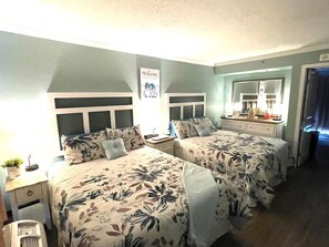 Ein Hotelzimmer mit zwei Betten, einem Nachttisch mit Lampe, einem kleinen Tisch mit Pflanze und einem Spiegel über dem Schminktisch.