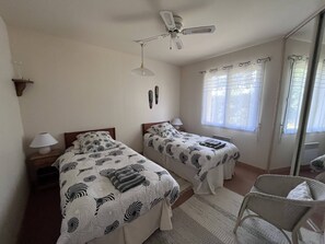 A bedroom with two beds, a ceiling fan, a window with curtains, and a chair. - Gîte Le Clocher du Layon (Nueil Sur Layon)