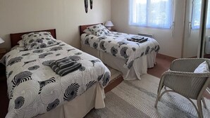 Ein Schlafzimmer mit zwei Betten, einem Deckenventilator, einem Fenster mit Vorhängen und einem Sessel.