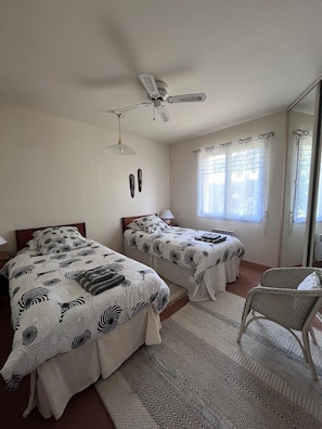 A bedroom with two beds, a ceiling fan, a window with curtains, and a chair. - Gîte Le Clocher du Layon (Nueil Sur Layon)