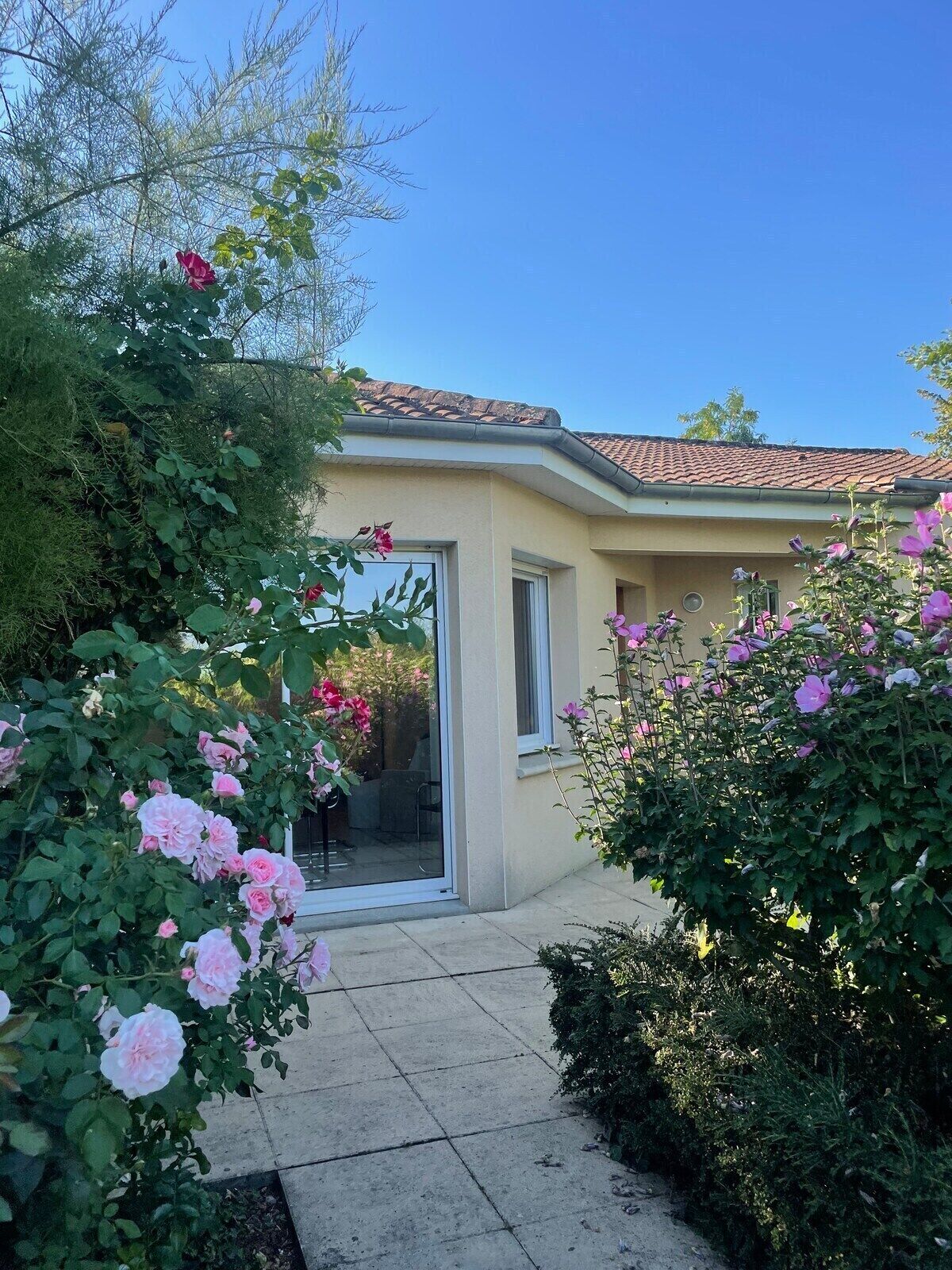 A house with a tiled roof, a glass door entrance, and a garden with pink and purple flowers.